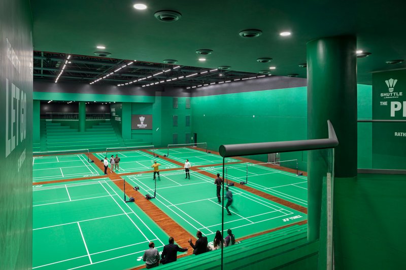 Interior view of green-walled badminton courts with players and spectators beneath recessed ceiling lighting
