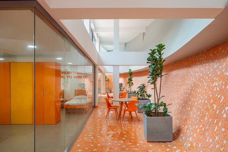 Interior corridor with orange terrazzo flooring, glazed office partitions, potted plants and orange seating under skylights