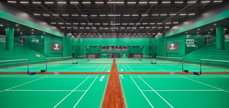 Badminton courts with green playing surface and mint walls under a black ceiling grid with linear lighting
