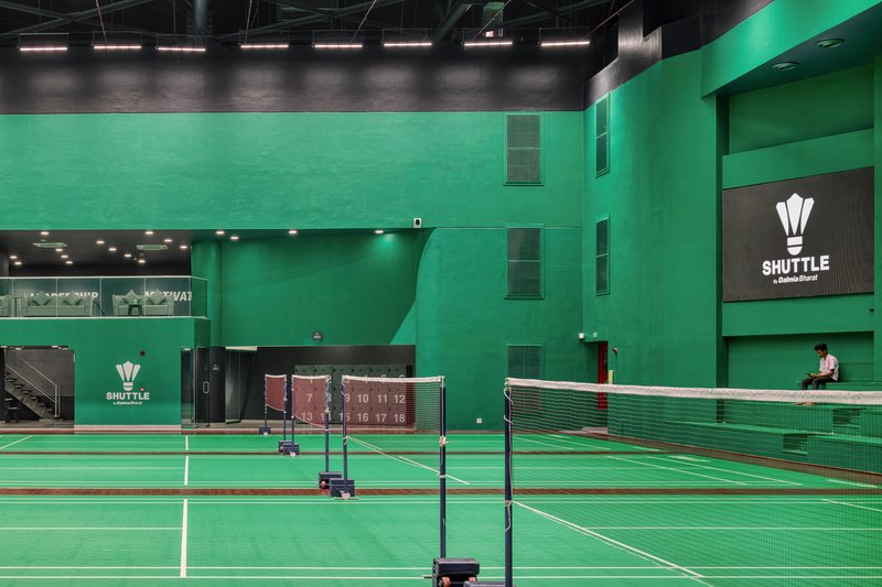 Multi-level sports hall interior with green walls, badminton nets, and a lone figure on the upper level