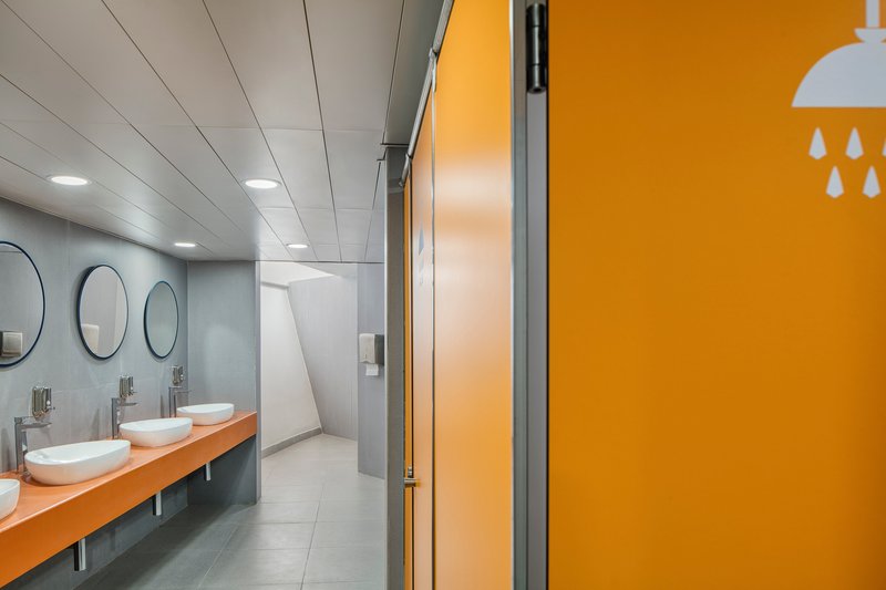 Washroom with three round mirrors above white vessel sinks on a timber counter and yellow partition panels
