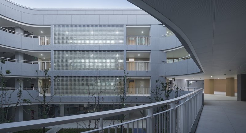 Translucent glass block facade framed by curving circulation balconies with young trees below