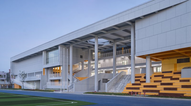 Athletic field beside a raised volume with exposed columns and timber bleachers at twilight
