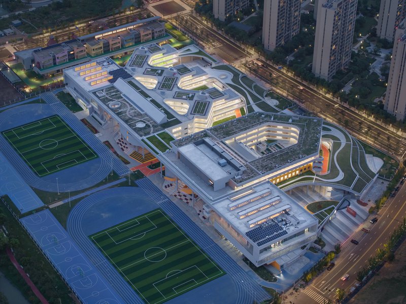 Drone view of the layered white roofs with solar panels and adjacent football pitches at twilight
