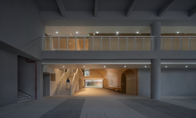 Interior lobby with timber-lined arched passage and sculptural staircase beneath a grey concrete ceiling