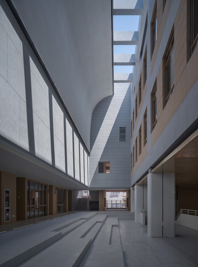 Courtyard view between white panel facades with skylight bands above and a curved volume beyond