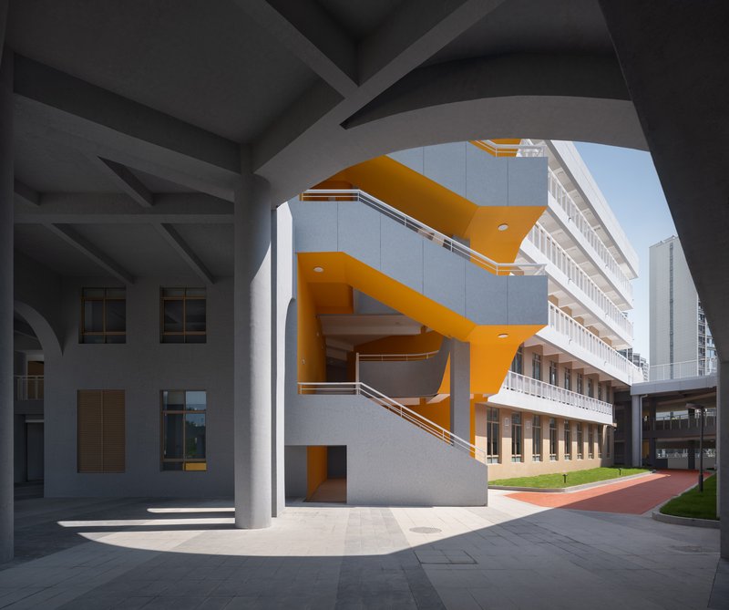 Covered entrance courtyard with orange zigzag staircase against white facade under exposed concrete beams