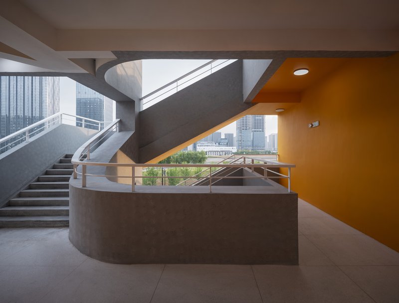 Curved concrete staircase with orange soffit and metal railing framing view toward athletic fields