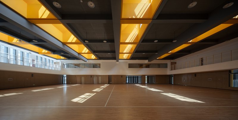 Gymnasium floor with timber surface beneath alternating grey and yellow coffered ceiling panels in sunlight