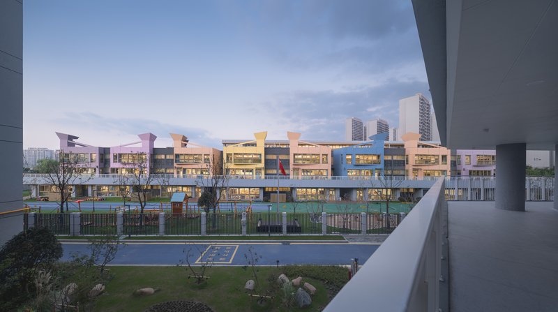 View across landscaped courtyard toward illuminated facades and colorful canopy elements at dusk