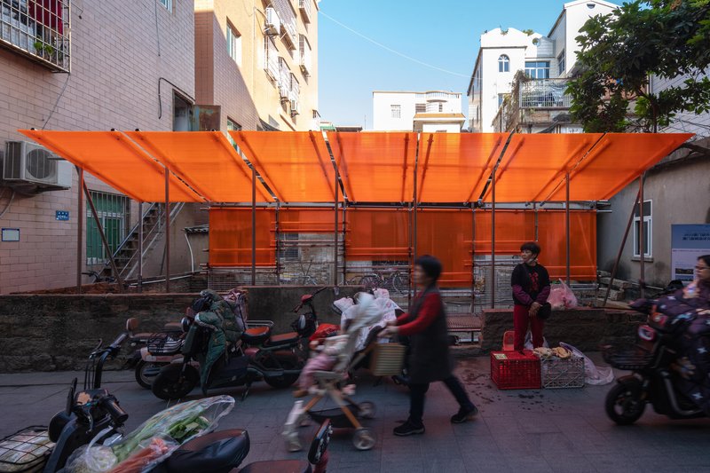 Street-facing view of the translucent orange canopy with pedestrians and motorbikes passing beneath