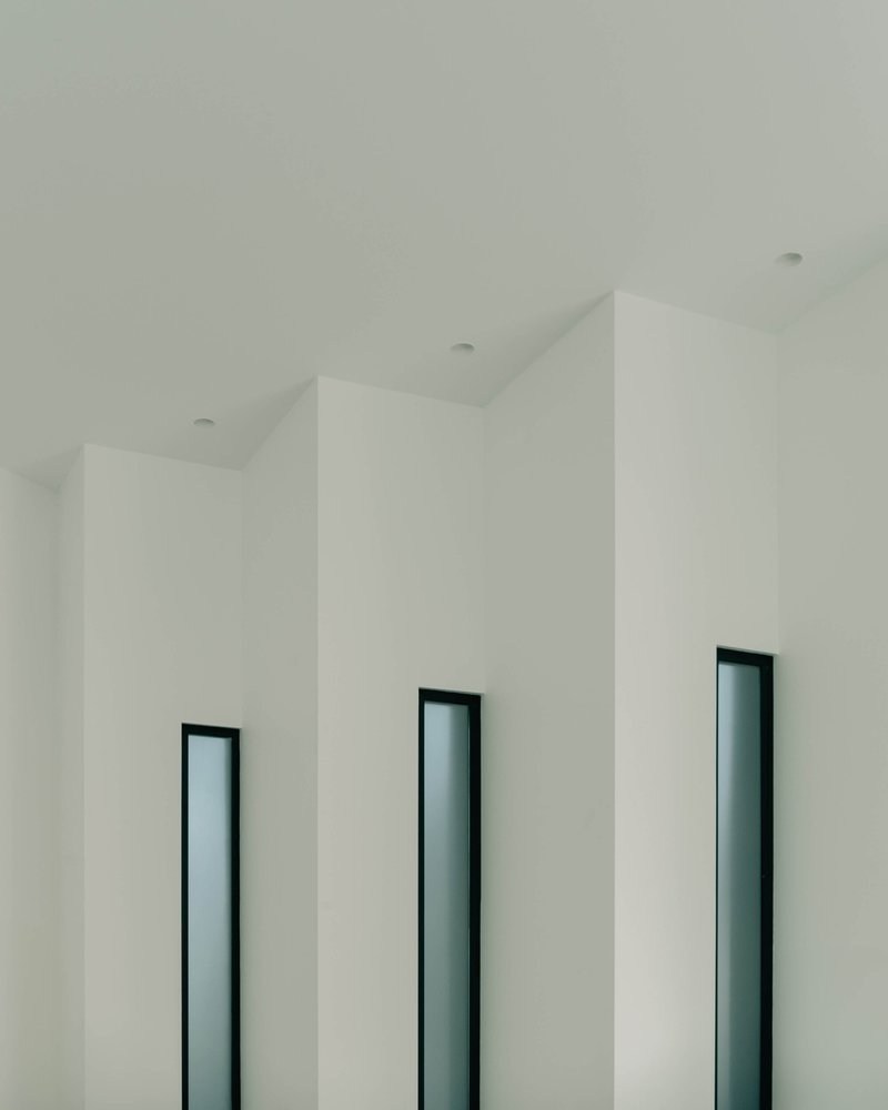 Three vertical window openings with dark frames set into white folded ceiling planes