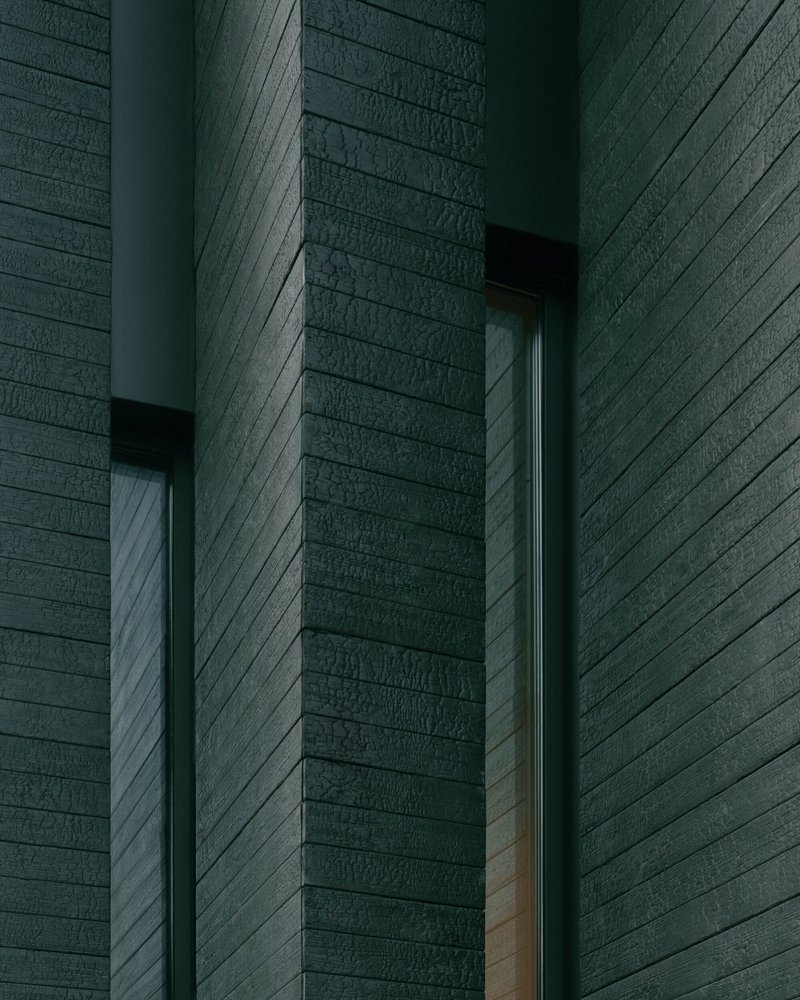 Close-up of horizontal timber cladding meeting at a recessed corner with narrow window openings