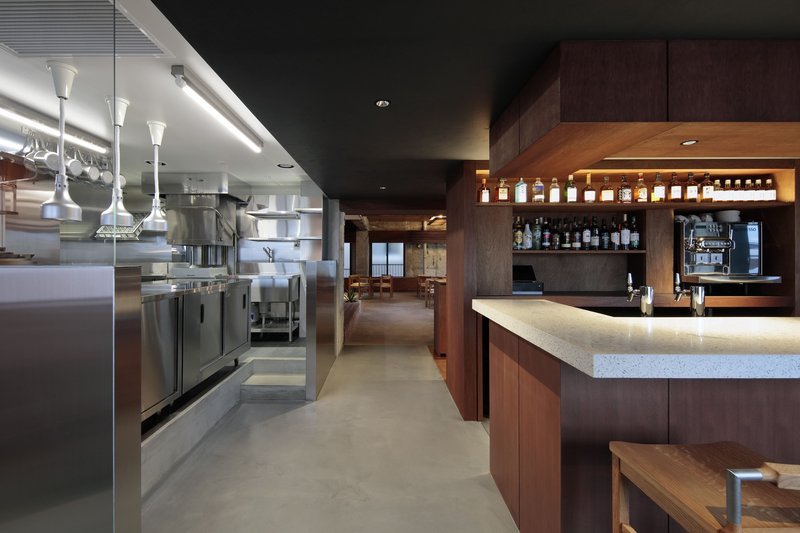Restaurant interior with stainless steel kitchen equipment and walnut bar counter under linear ceiling lights