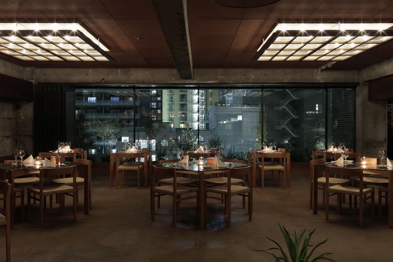 Dining room with wooden tables set for service beneath illuminated ceiling panels at night