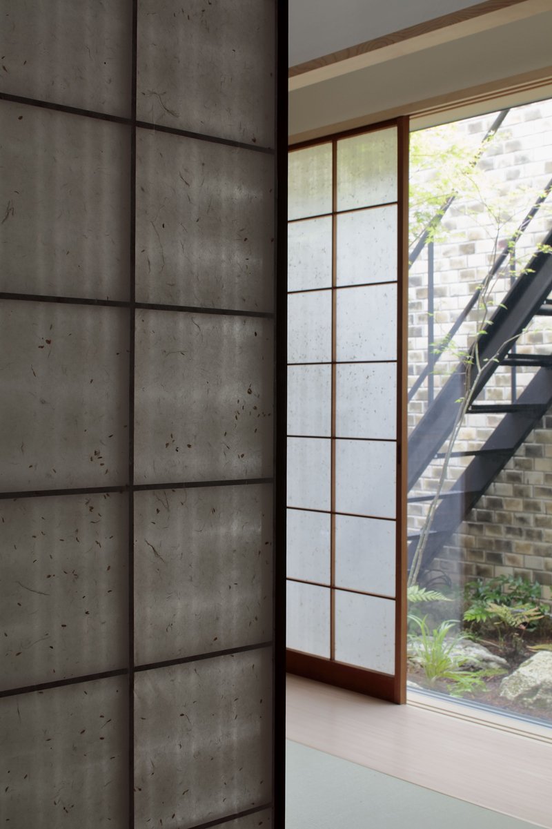 Shoji screen and board-formed concrete wall beside a courtyard garden with steel stair