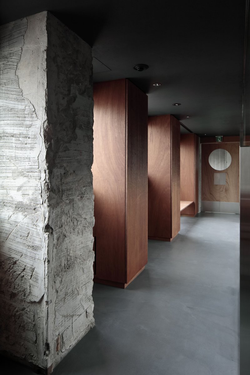 Corridor with freestanding timber partitions alongside an exposed concrete column under recessed ceiling lights