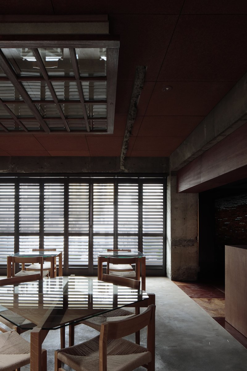 Dining chairs beside floor-to-ceiling louvered screens filtering daylight into concrete and timber interior
