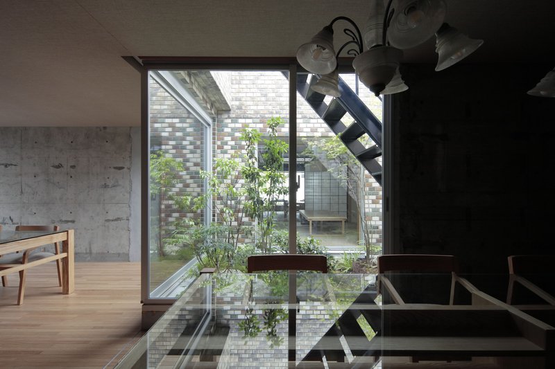 Interior courtyard with glass block walls and planted trees viewed through floor-to-ceiling glazing and steel staircase