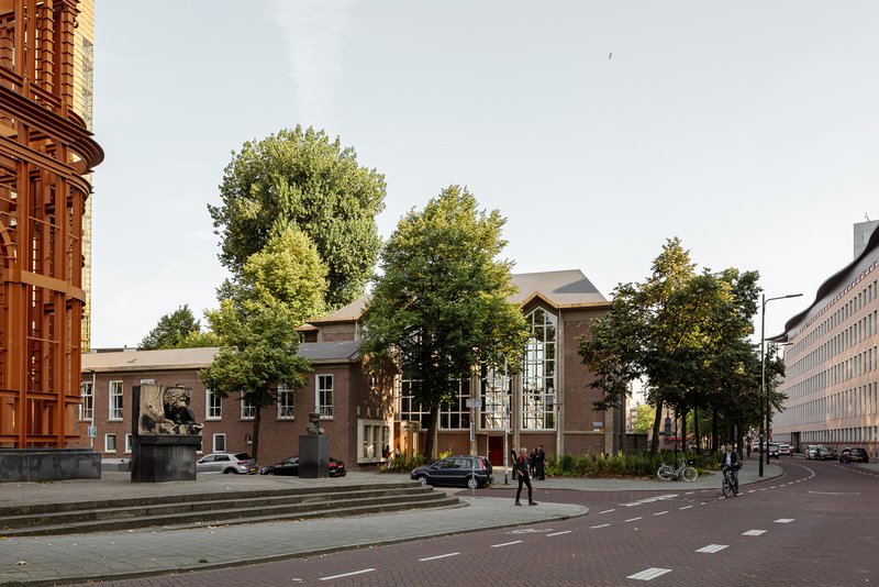 Street view of the brick facade with arched glazing and mature trees in dappled afternoon light