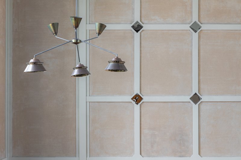 Multi-arm chandelier hanging against wall panel grid with diamond-shaped glass inserts and white trim