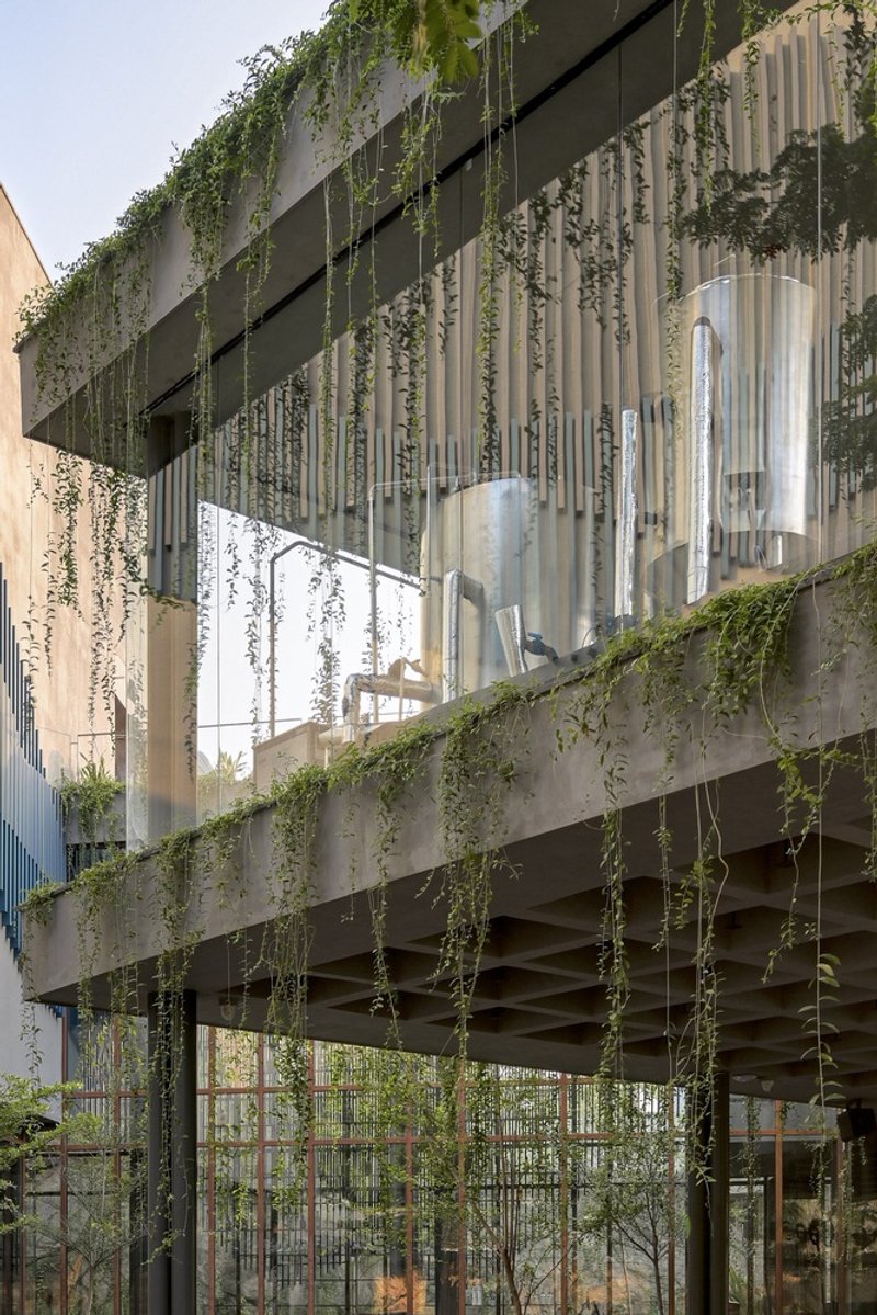 Concrete facade with vertical metal fins and cascading vegetation from the planted terrace above