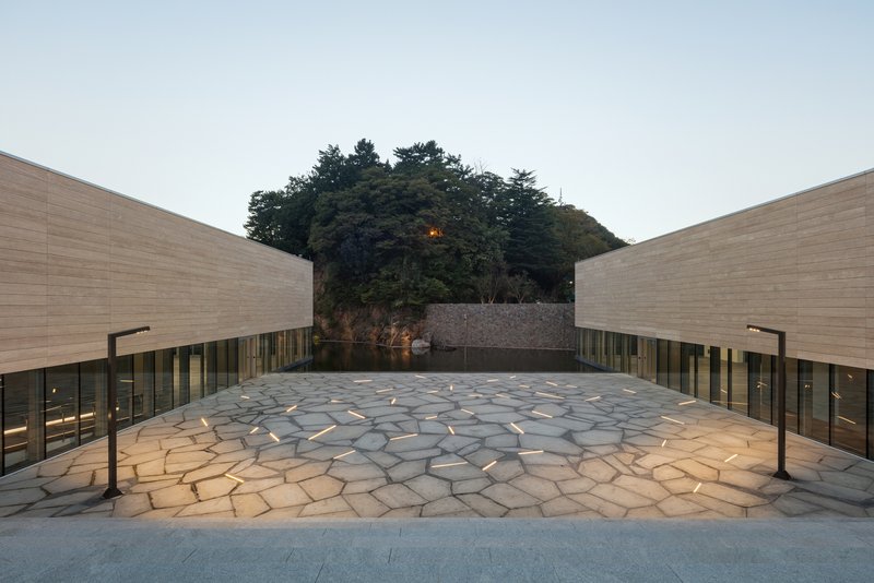 Stone-paved courtyard between two wings with a tree-covered hill beyond at twilight