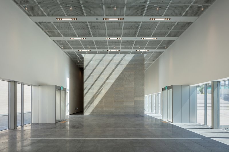 Gallery interior with perforated metal ceiling and sunlight casting diagonal shadows on the wall
