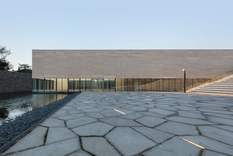 Low-angle view of the polygonal stone paving extending toward glass facade at twilight