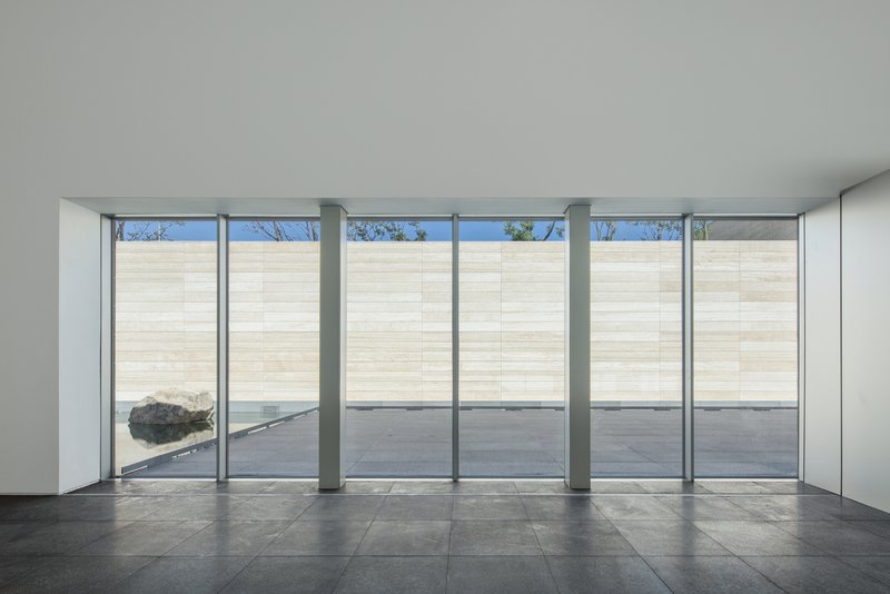 Interior gallery space with floor-to-ceiling glass walls facing a pale stone courtyard wall