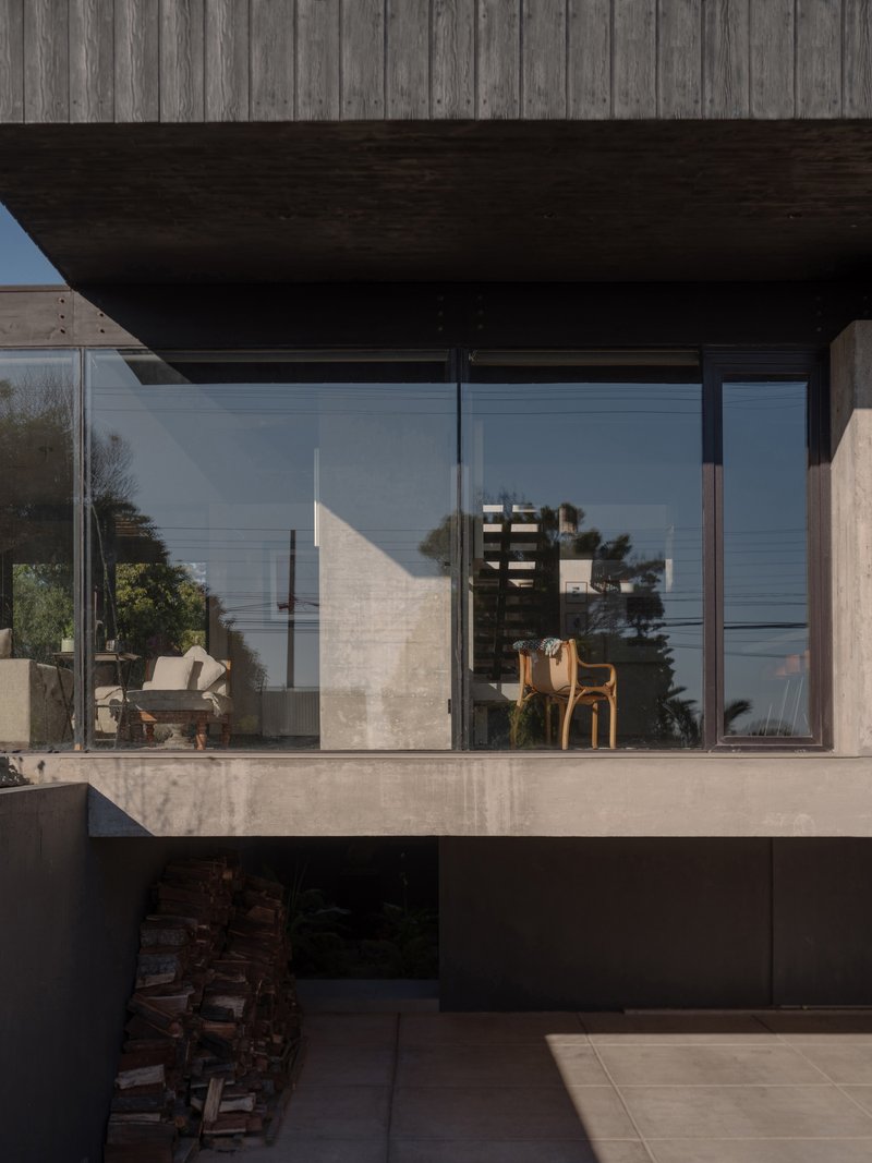Full-height glazing beneath dark timber soffit reflecting concrete walls and furnishings in afternoon light