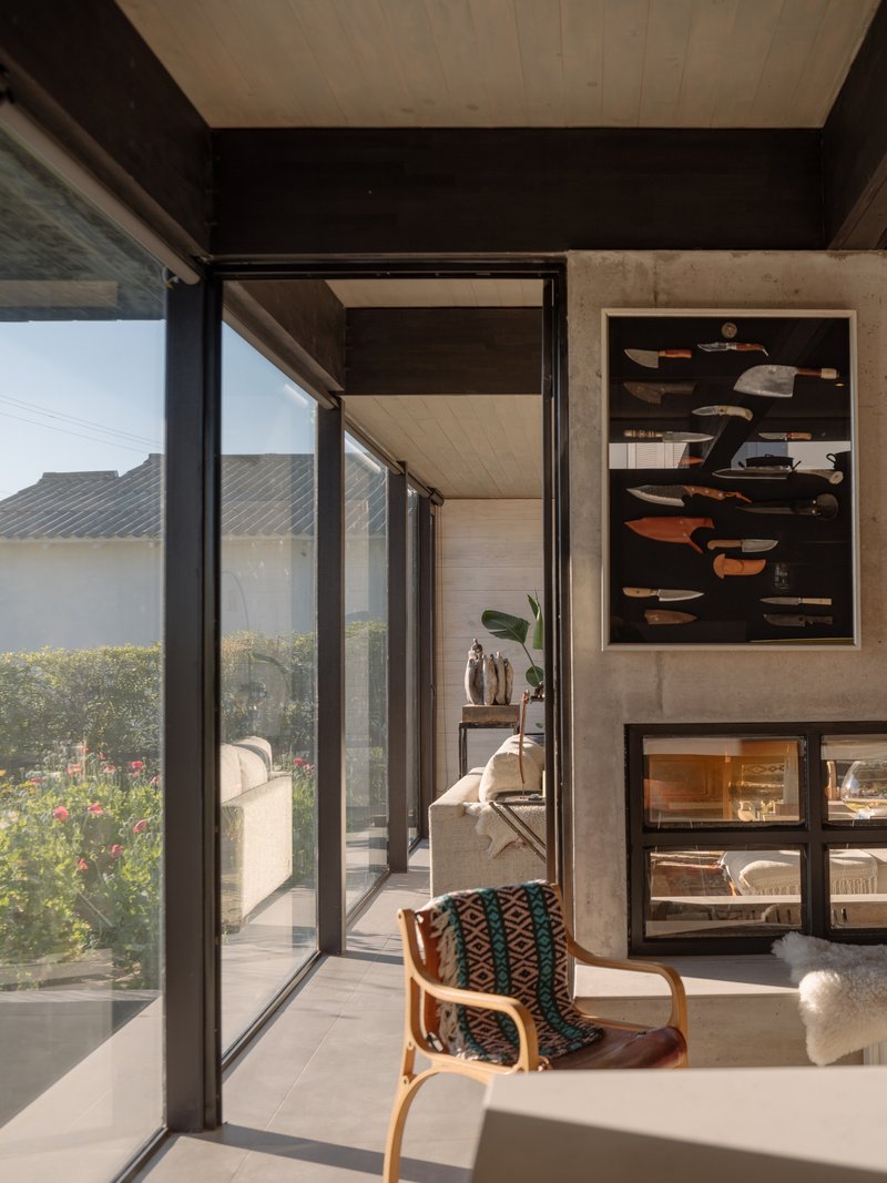 Interior corner with black steel framed glazing opening to a planted terrace in afternoon light