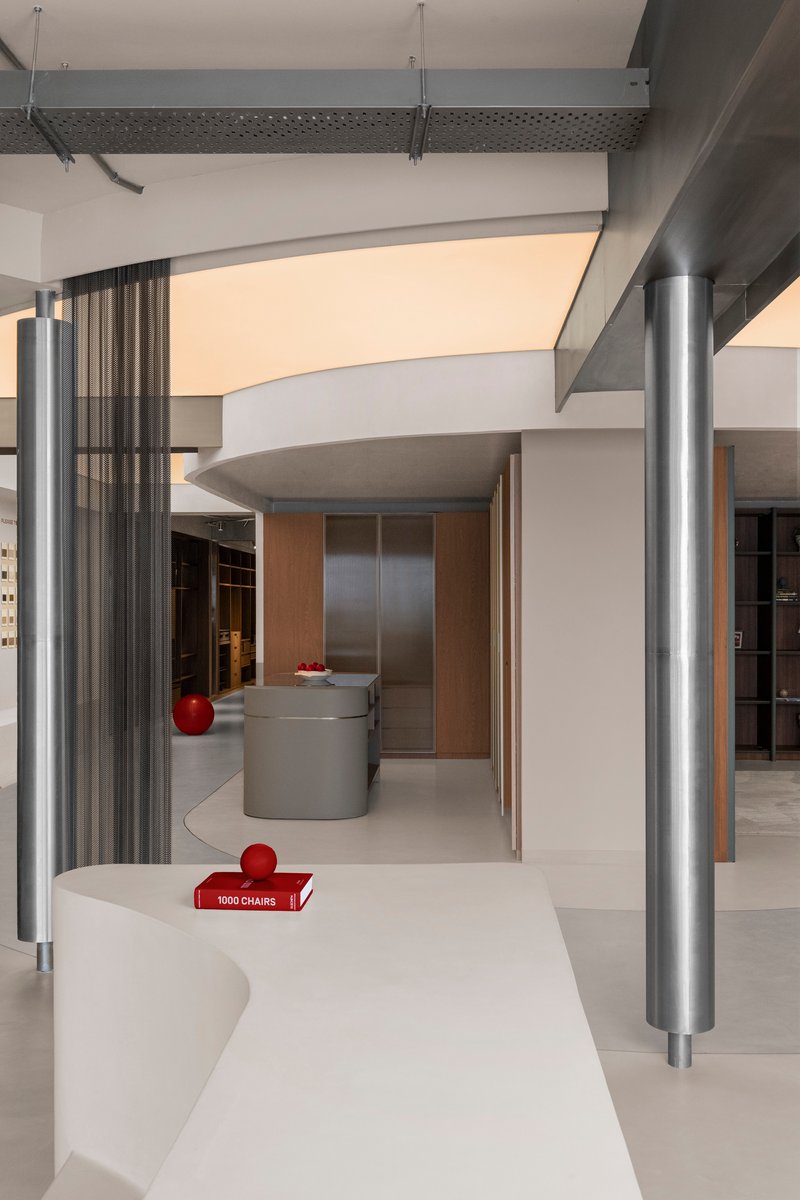 Curving white display counter with metal columns and overhead beams in a retail space