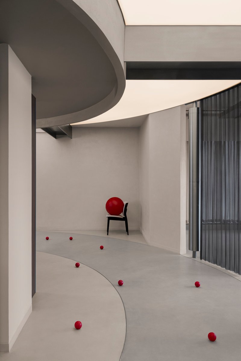 Gallery space with scattered red balls on curved floor sections and a black chair against the wall