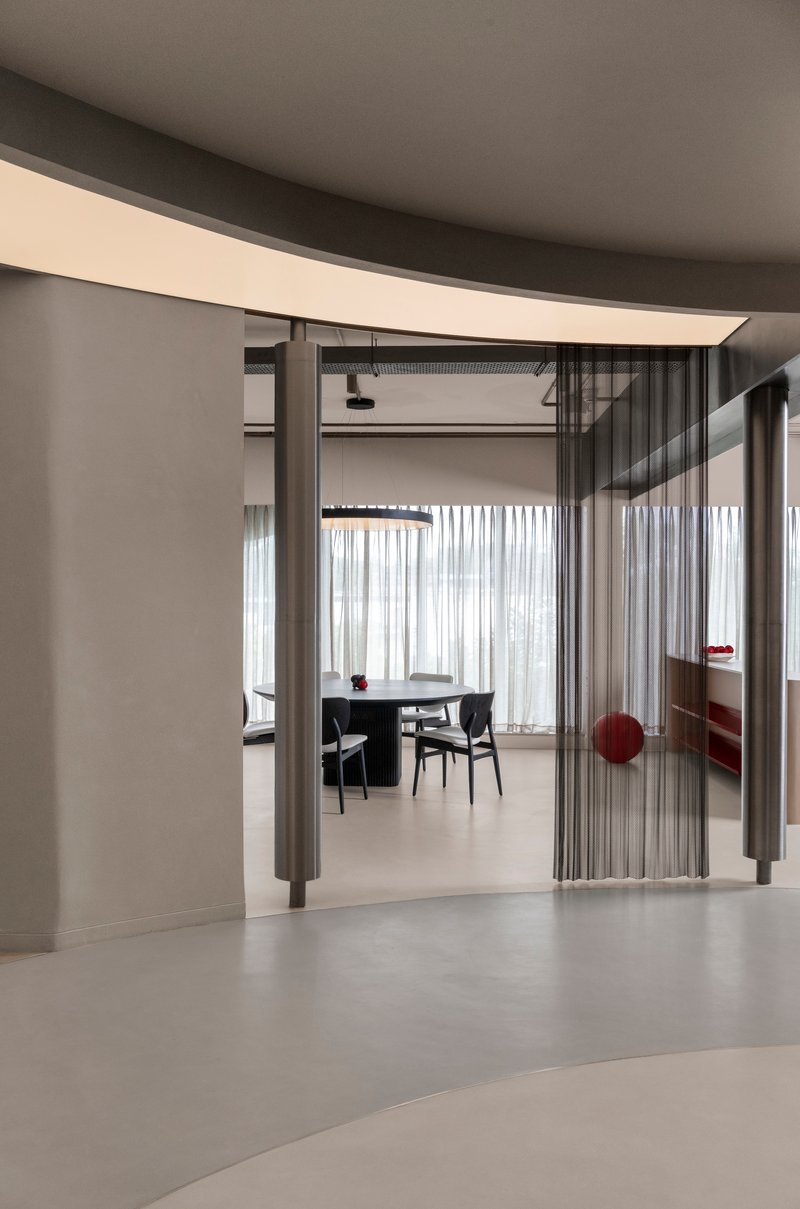 View through a folding metal screen partition into a dining area with sheer curtains and concrete floors