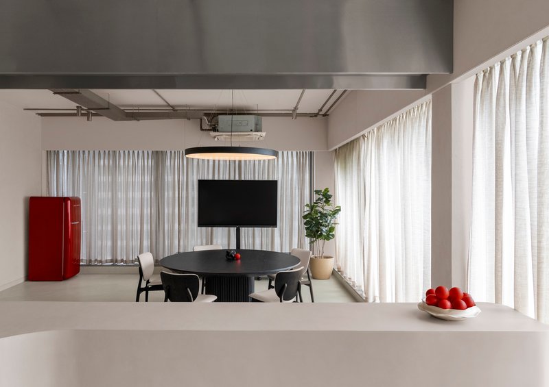 Open plan dining space with white curtains, exposed ceiling ducts, and a red refrigerator at the perimeter