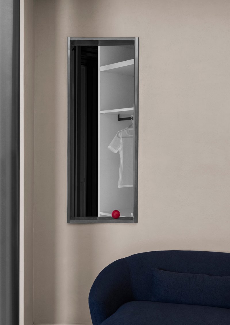 Tall narrow aperture in the wall framing a view into a wardrobe with hanging garment