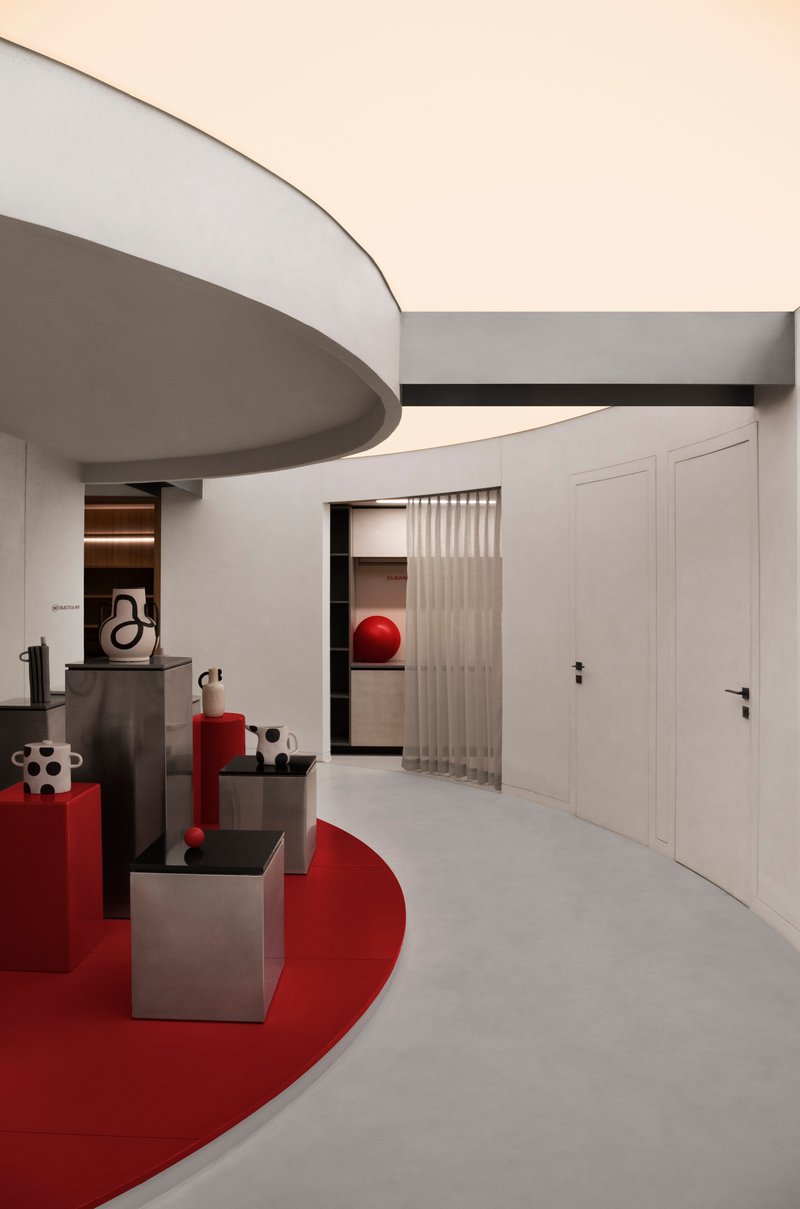 Curved ceiling edge above a red floor graphic with sculptural objects on grey pedestals