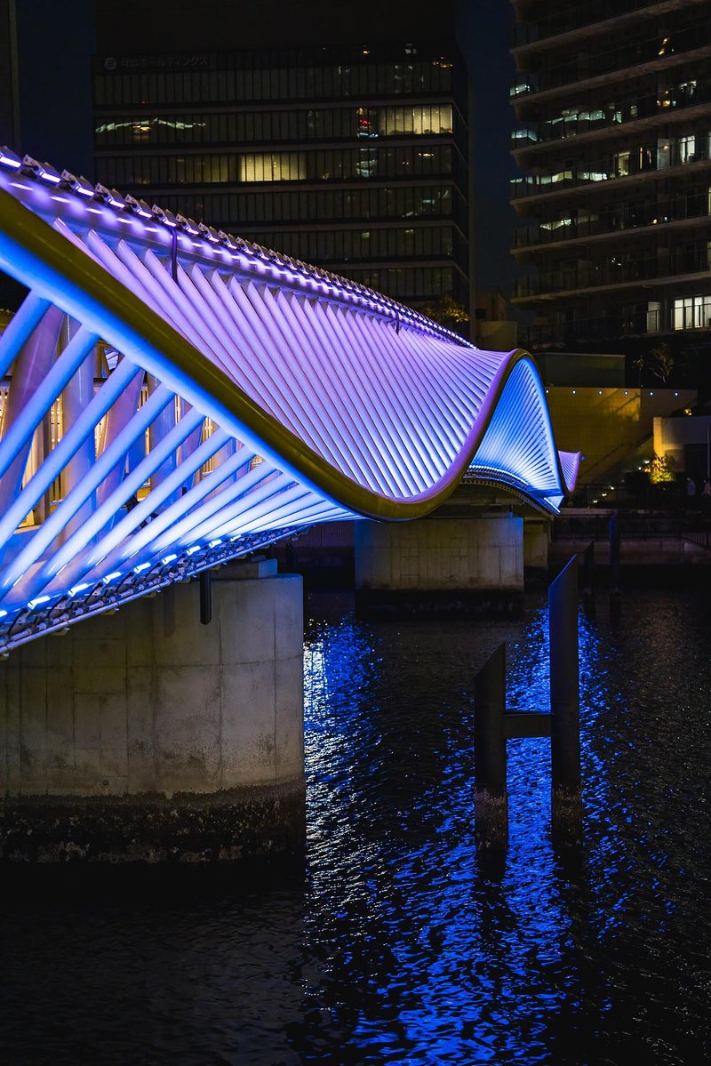 Close view of the bridge's wavelike illuminated roof structure rising above concrete piers in water