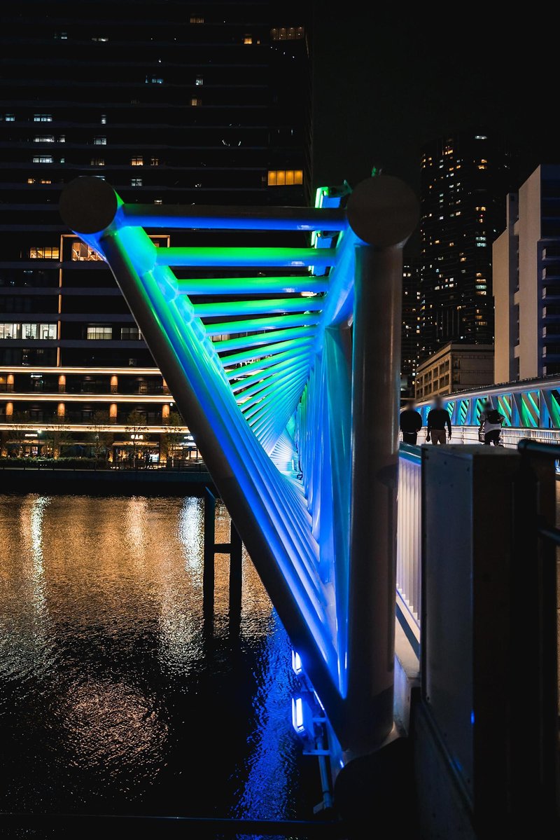 Twisted tubular steel truss structure glowing with gradient LED lighting at the bridge support