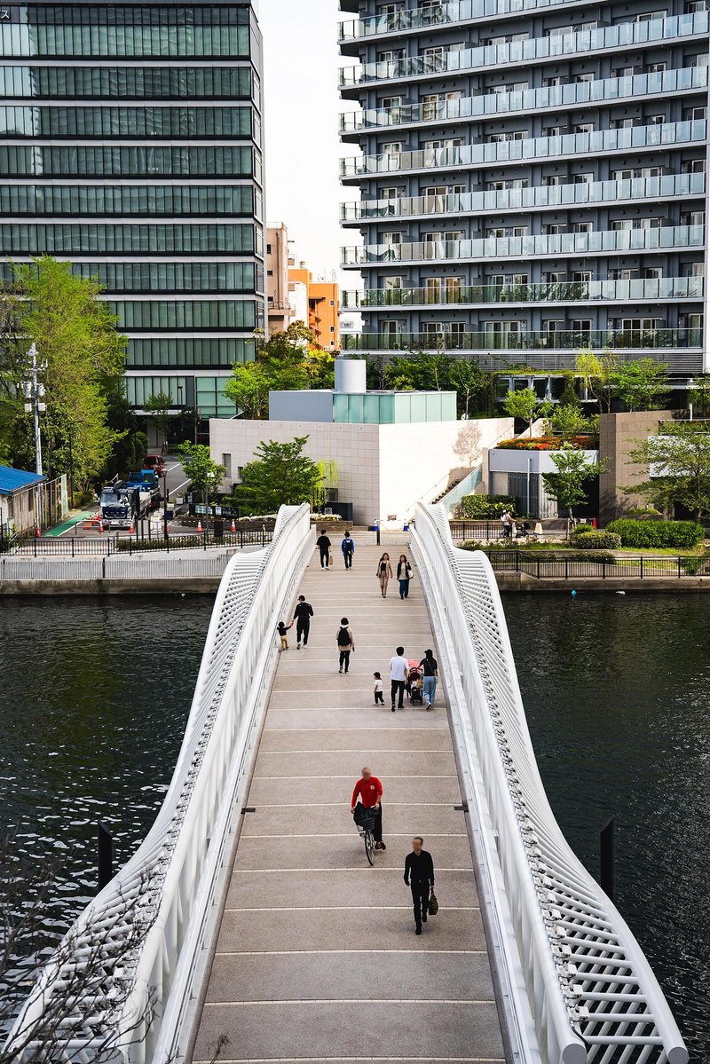 View along the timber deck of the bridge with pedestrians and cyclists moving between glass towers
