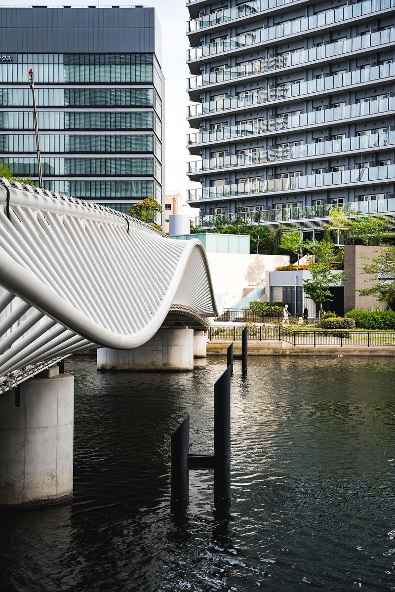 Curved white lattice roof structure of the bridge landing rising from concrete piers in the canal
