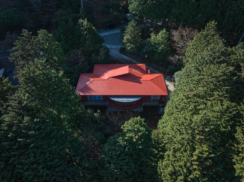 Aerial view of the red tiled roof with a curved center element nestled among dense forest canopy