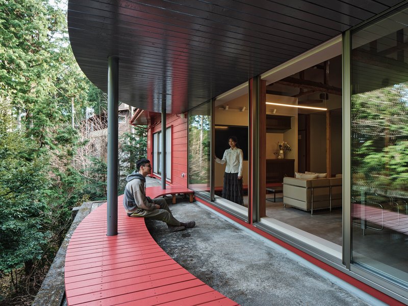 Covered deck with red planks and black soffit where two figures gather near sliding glass doors