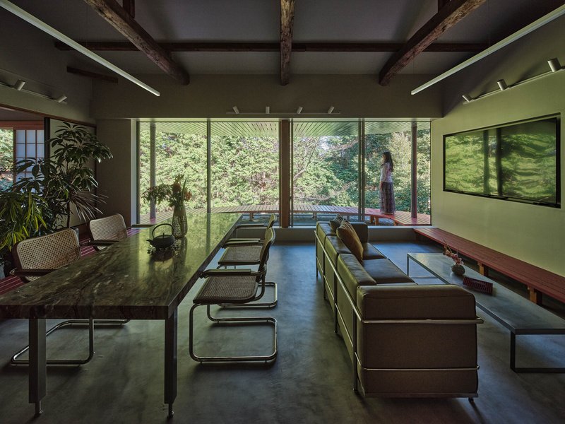 Interior living space with exposed timber beams and floor-to-ceiling glazing overlooking garden with figure standing outside