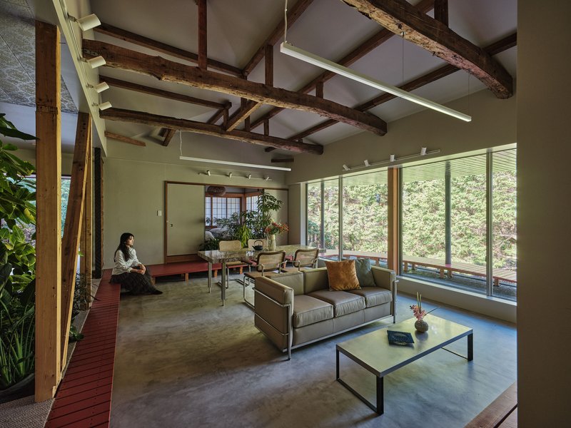 Living room with polished concrete floor and exposed timber ceiling beams with person seated on red platform