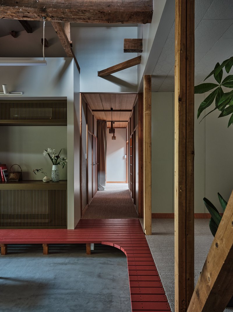 Raised red timber platform connecting interior spaces with exposed ceiling beams and olive green walls
