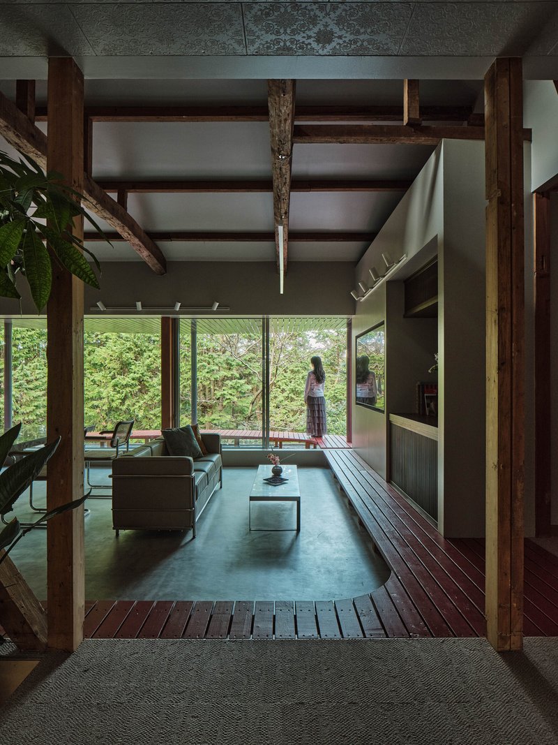 Living room with exposed timber frame and glass wall overlooking garden with figure standing outside