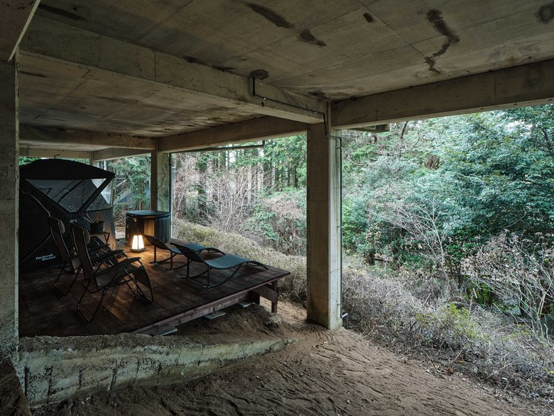 Covered outdoor terrace with concrete soffit and timber deck overlooking wooded hillside in afternoon light