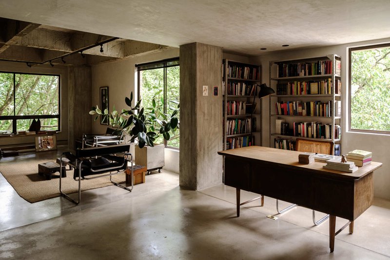Open living area showing concrete columns, timber joinery, and floor-to-ceiling windows overlooking greenery
